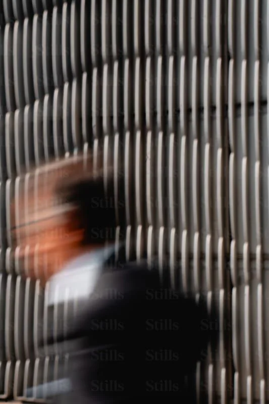 A person walking past ridged metal panels, in motion blur
